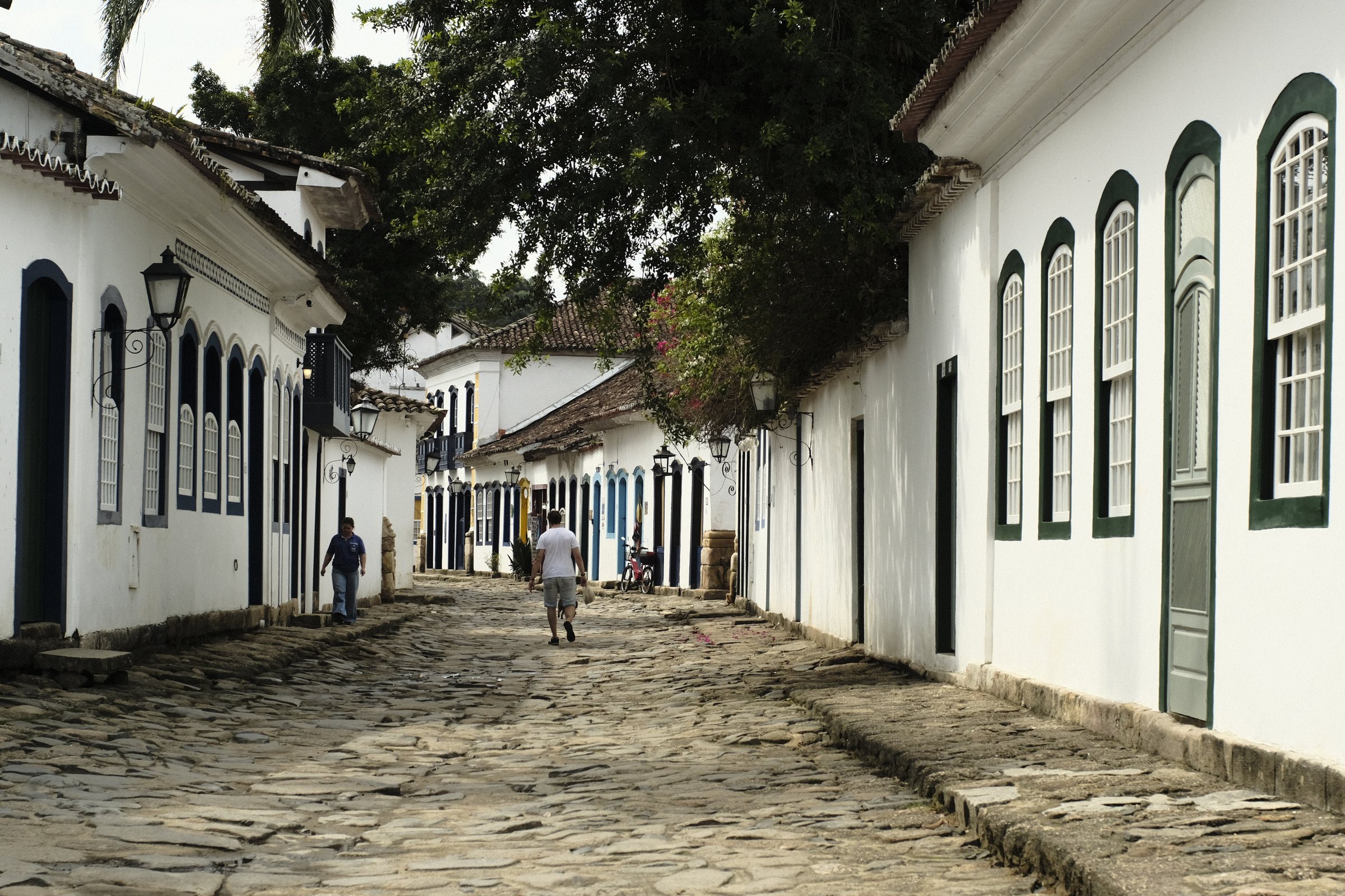 Person walking down a cobblestone street lined with white colonial houses in Paraty